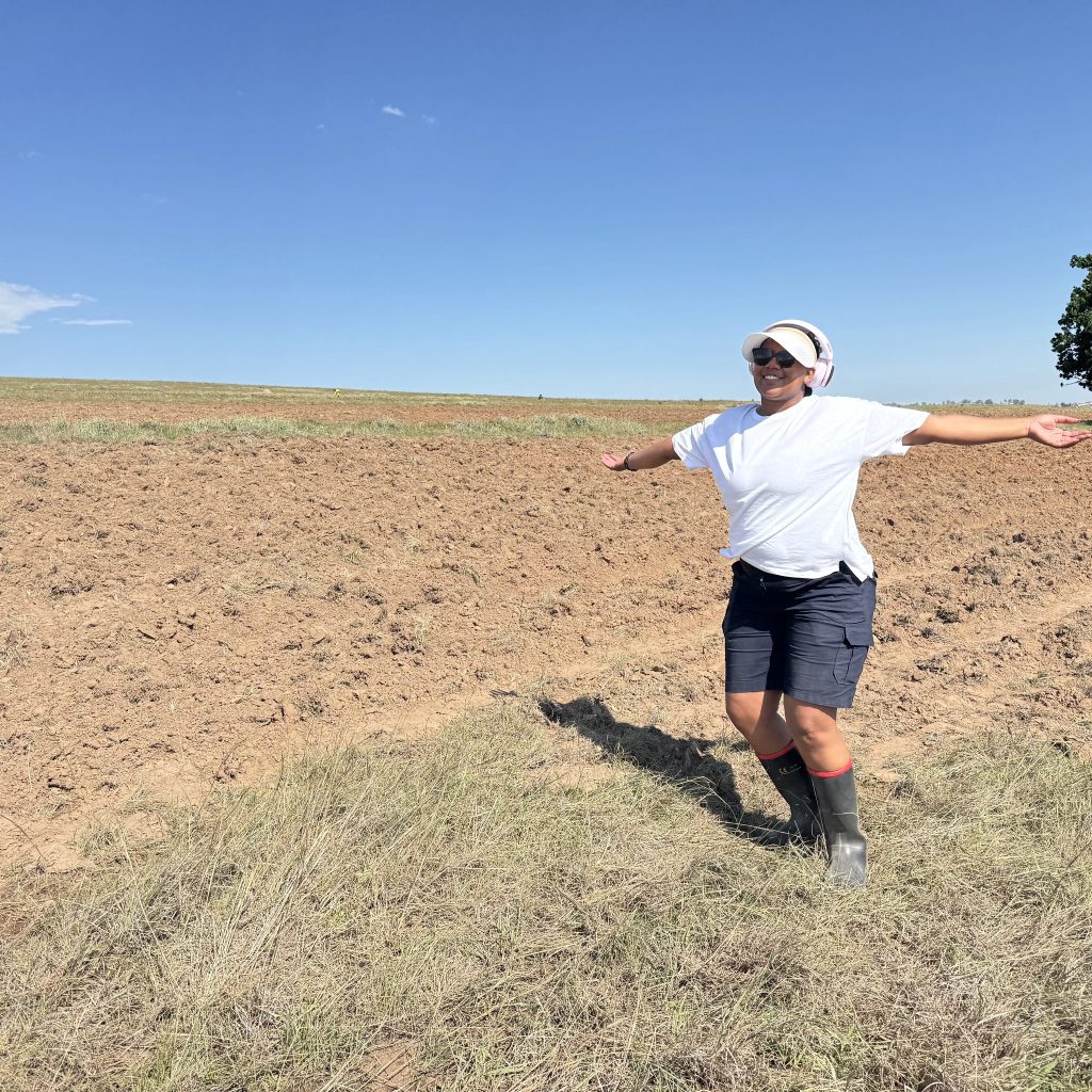 Woman with arms spread wide smiling on a ploughed field in Mount Frere, Eastern Cape